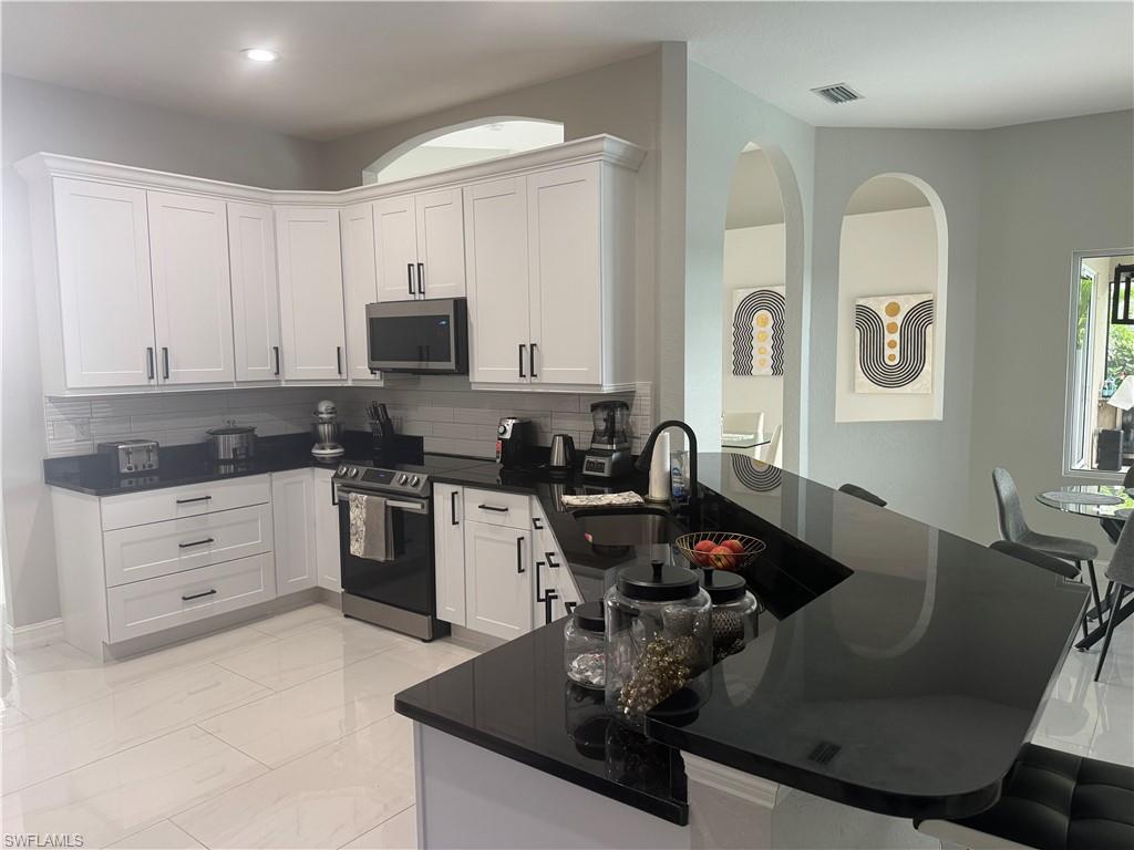 18445 Royal Hammock Boulevard Naples, FL 34114 - Photo 22 of 50 Kitchen featuring stainless steel appliances, white cabinets, a kitchen bar, a peninsula, and dark stone countertops