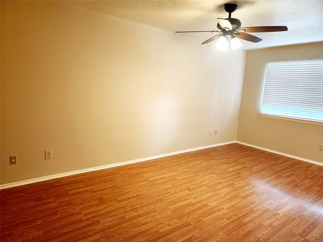 an empty room with wooden floor fan and windows