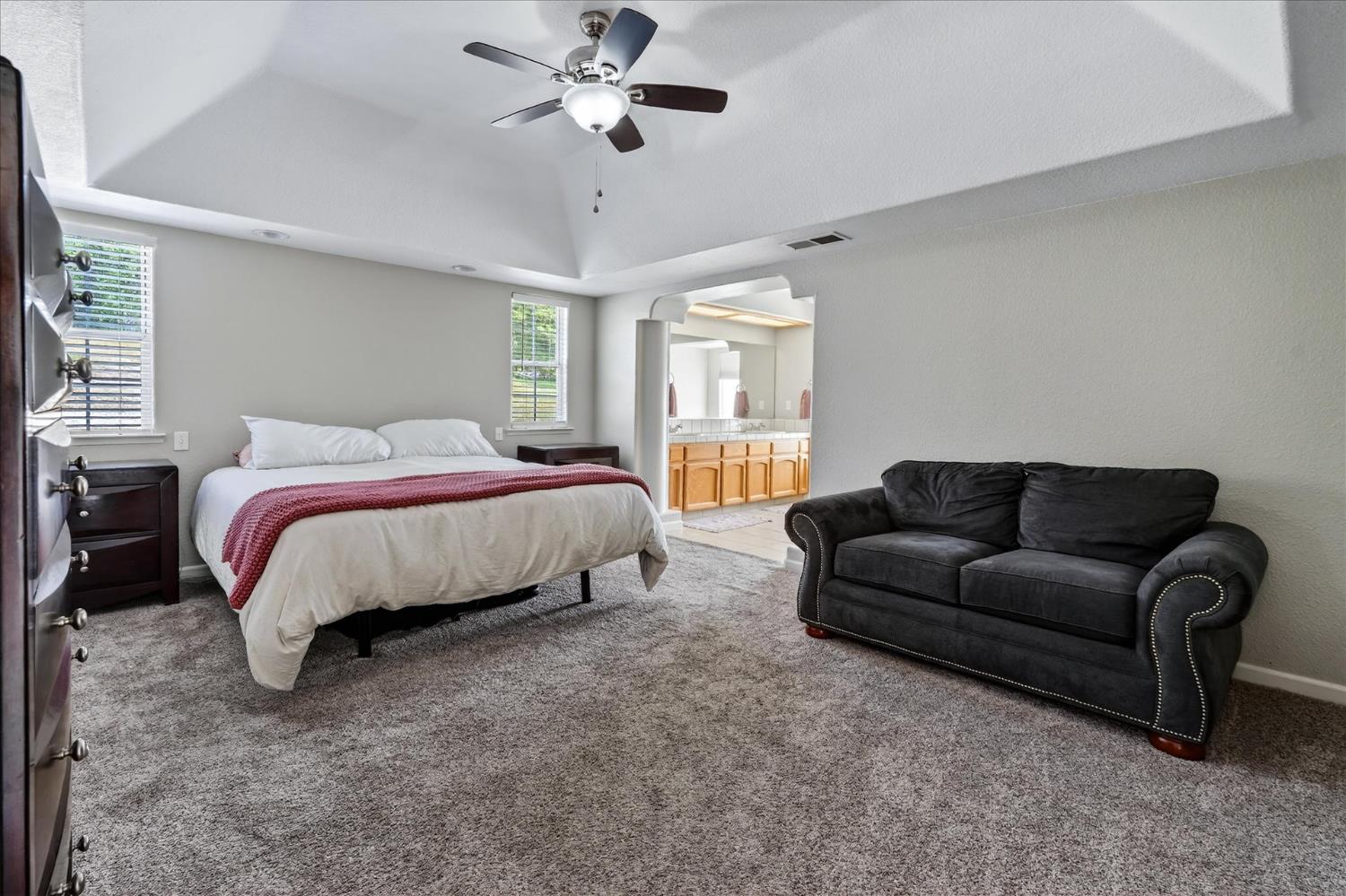 47482 Veater Ranch Road Coarsegold, CA 93614 - Photo 29 of 51 a spacious bedroom with a bed couch chandelier windows and a ceiling fan