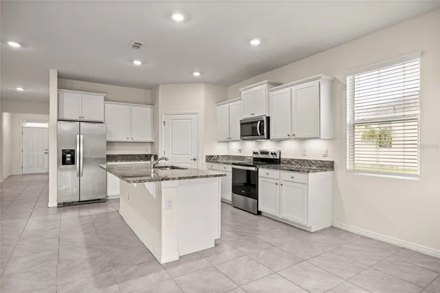 a kitchen with stainless steel appliances granite countertop a stove top oven a sink a refrigerator and white cabinets
