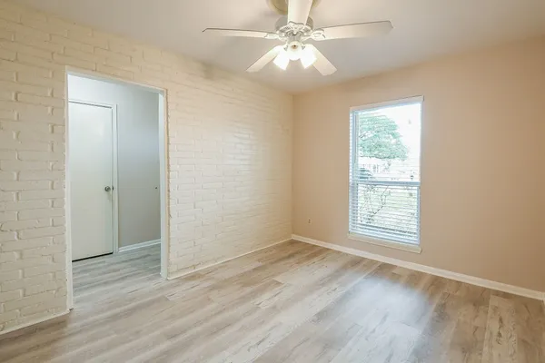 an empty room with wooden floor fan and windows