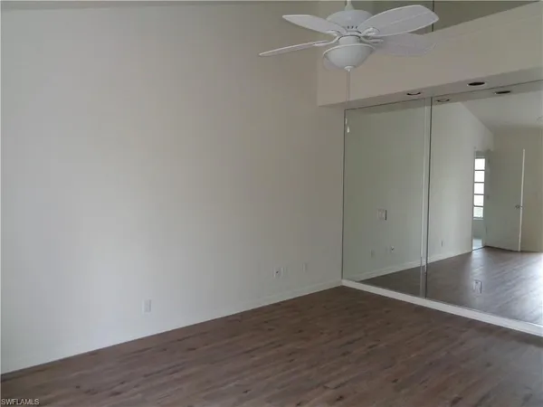 a view of an empty room with wooden floor and a ceiling fan