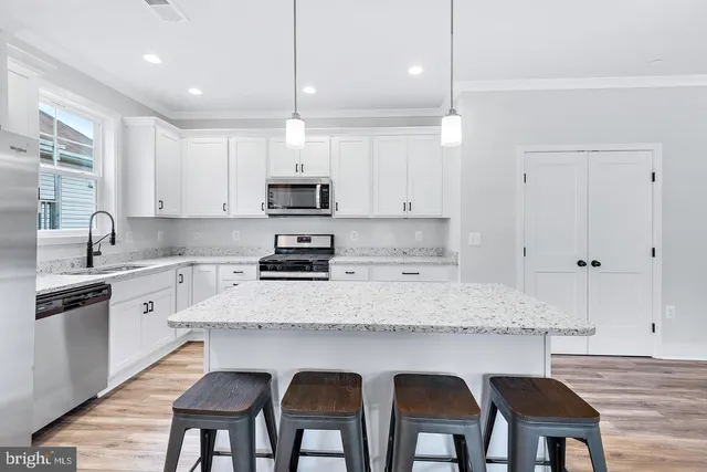 a kitchen with stainless steel appliances granite countertop a stove a sink a microwave a refrigerator white cabinets and chairs