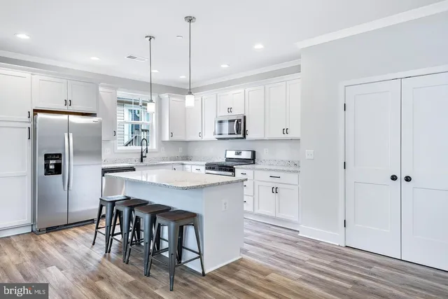 a kitchen with stainless steel appliances granite countertop a refrigerator a sink dishwasher a stove and white cabinets with wooden floor