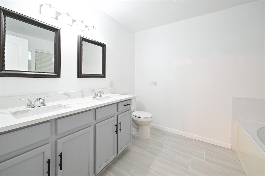 910 Rocking Spur Cove Pflugerville, TX 78660 - Photo 9 of 17 A well-lit primary bathroom featuring a double vanity, pristine white countertops, and contemporary gray cabinetry.