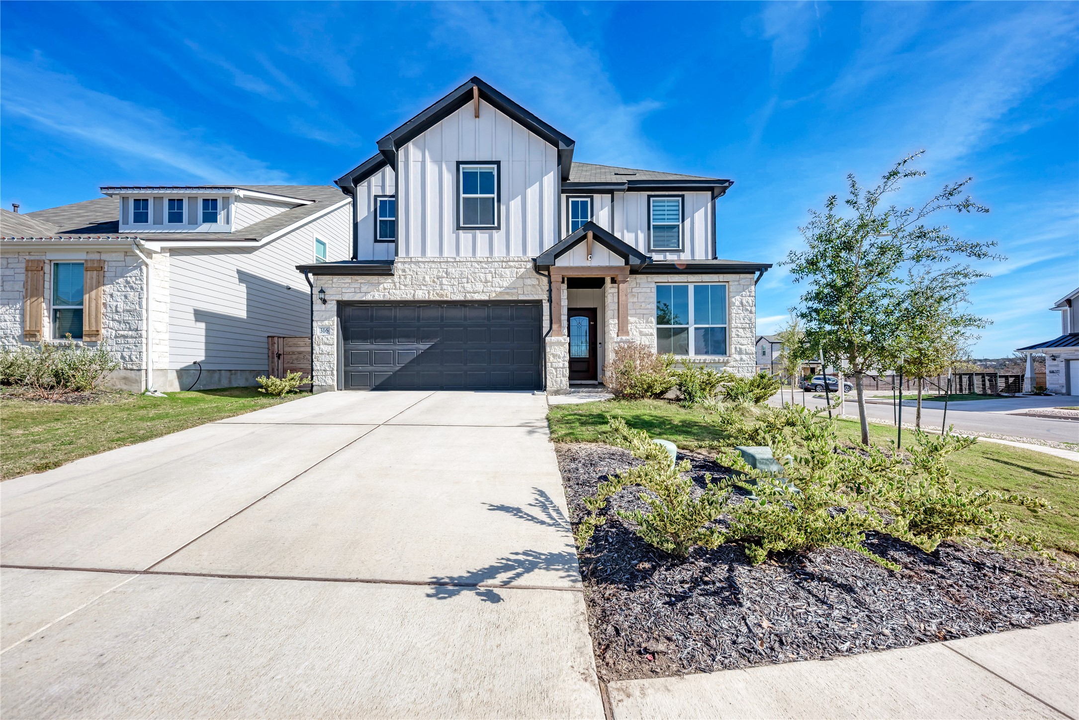 316 Regatta Trail Leander, TX 78641 - Photo 2 of 39 Contemporary two-story residence featuring a stone and board-and-batten facade, a two-car garage with a dark door, and a covered entry