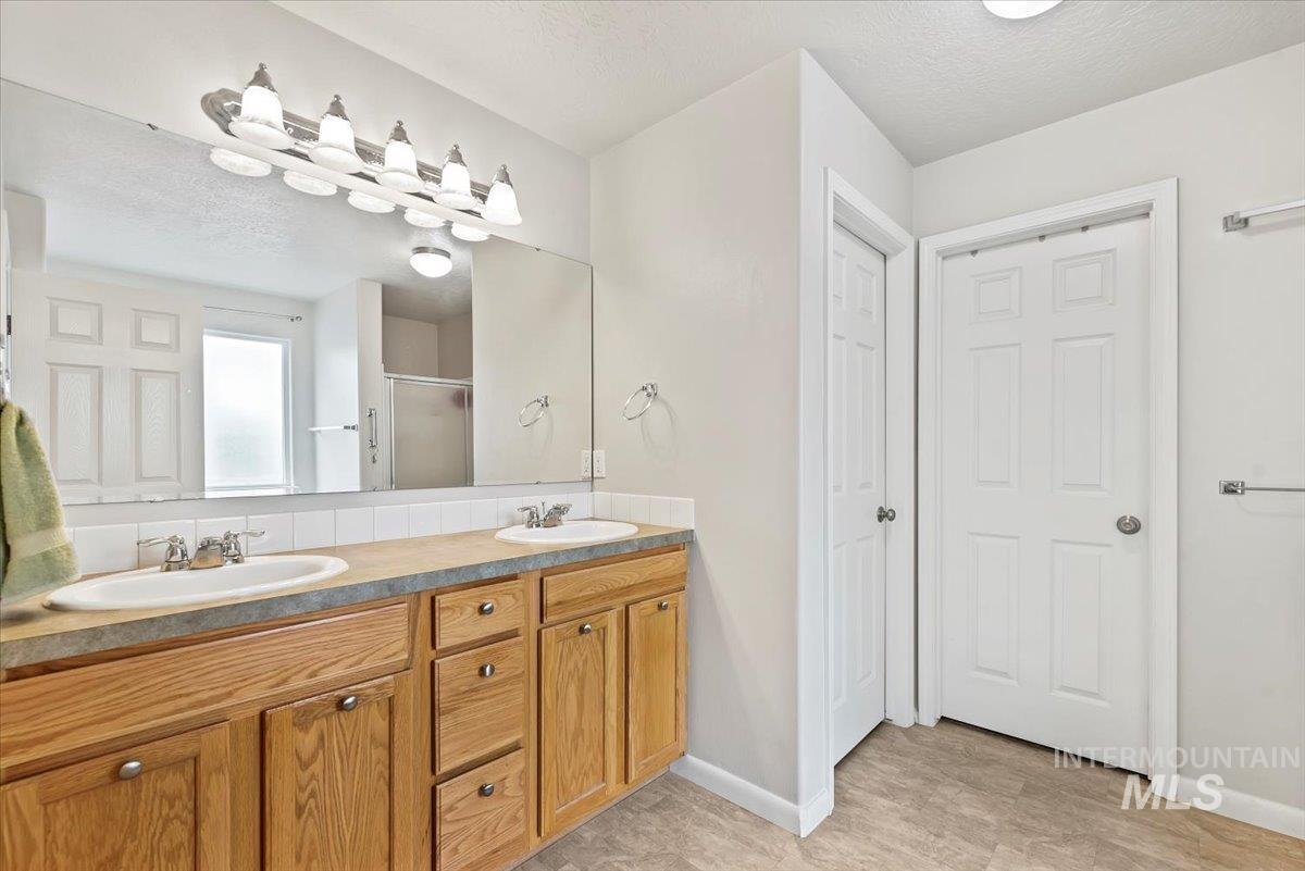 16608 Old Friendship Way Caldwell, ID 83607 - Photo 16 of 32 Full bathroom featuring a textured ceiling, double vanity, a stall shower, and a closet