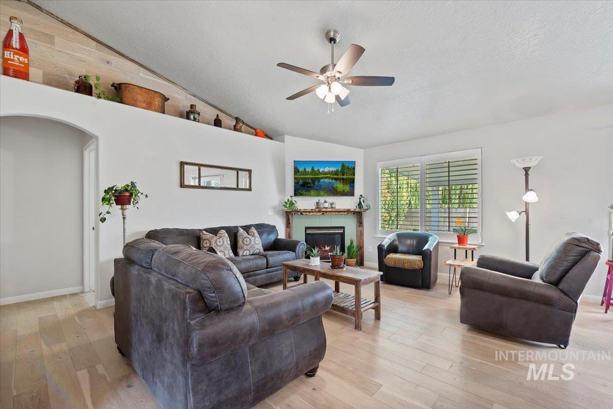 16608 Old Friendship Way Caldwell, ID 83607 - Photo 6 of 32 Living area featuring light wood-type flooring, a textured ceiling, vaulted ceiling, a warm lit fireplace, and ceiling fan