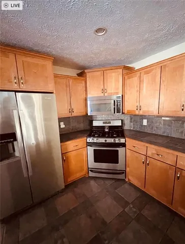 a kitchen with granite countertop a refrigerator a sink a stove a microwave a counter and cabinets