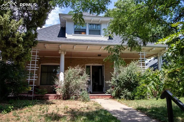 front view of a house with potted plants and large trees