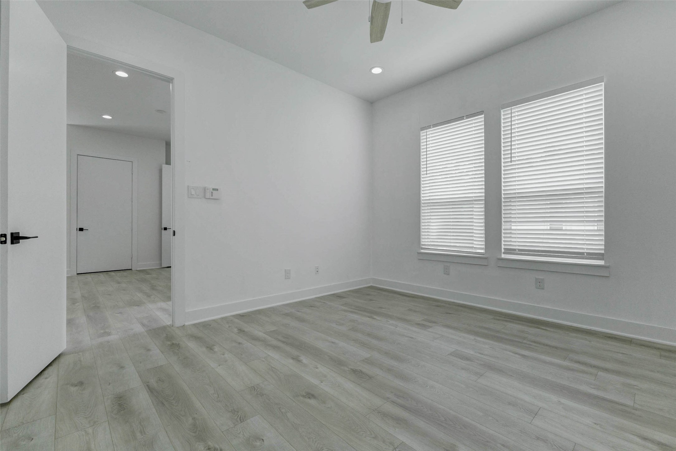 5705 Elysium Street Houston, TX 77091 - Photo 19 of 22 Primary bedroom with light wood-look flooring, tall ceilings, recessed lighting, and direct access to the en-suite bath. The clean white walls and open layout create a calm, modern retreat with plenty of flexibility for furnishings, while the visible glass shower adds a polished, private suite-style feel.