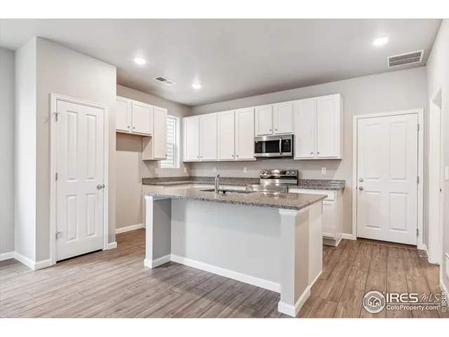 a kitchen with stainless steel appliances granite countertop a refrigerator a sink dishwasher a stove and white countertops with wooden floor