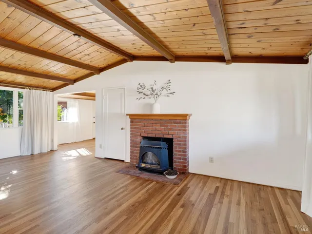 a view of an empty room with wooden floor fireplace and a window