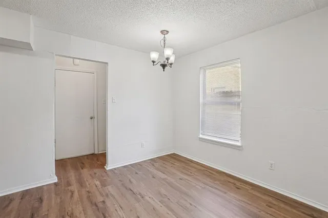 an empty room with wooden floor chandelier and windows
