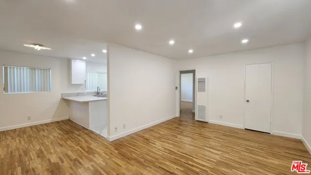 a view of an empty room with wooden floor and a kitchen