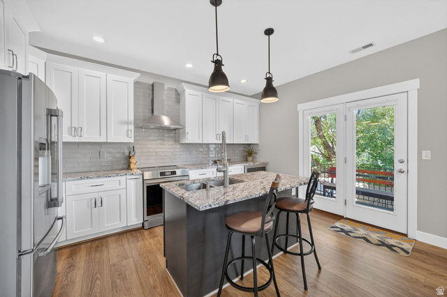 7872 Farm House Lane Midvale, UT 84047 - Photo 11 of 39 Modern kitchen featuring a central island with granite countertops and seating, stainless steel appliances, white cabinetry, and wood-finish flooring