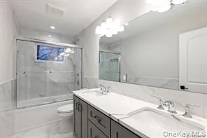 a bathroom with a granite countertop sink a toilet a mirror a vanity a bathtub and shower