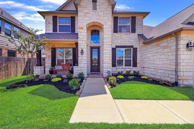 a view of a brick house with a yard plants and a large tree