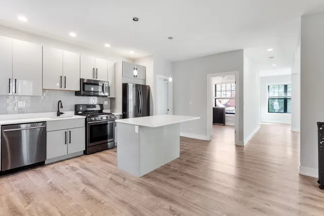 a kitchen with stainless steel appliances kitchen island granite countertop a stove a sink a refrigerator and white cabinets with wooden floor