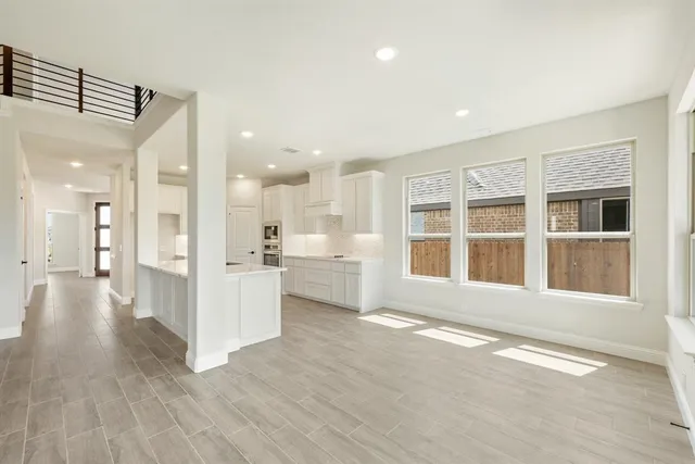 a view of an empty room with wooden floor and a kitchen