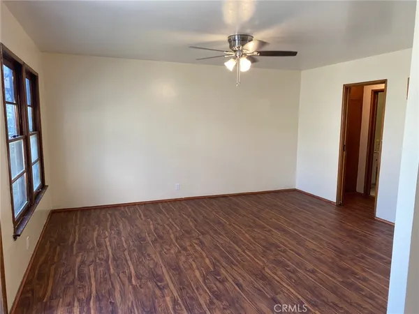 a view of an empty room with wooden floor and fan