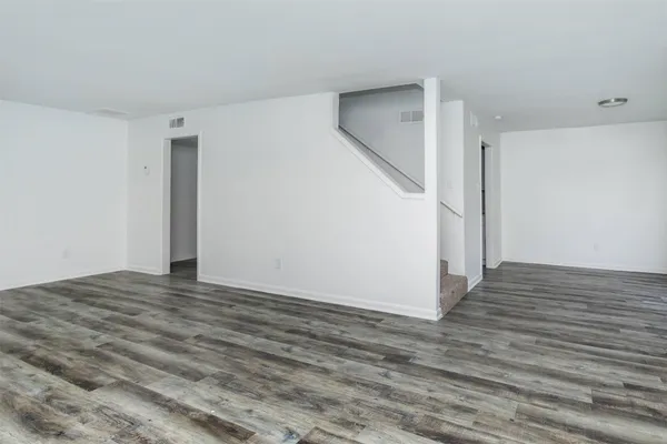 a view of an empty room with wooden floor and stairs