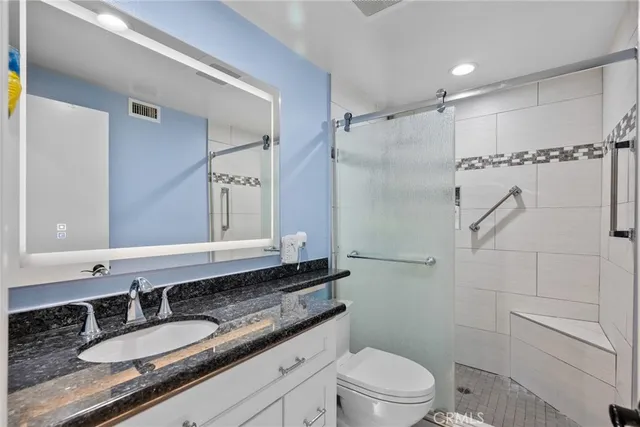 a spacious bathroom with a granite countertop sink a toilet a mirror and shower