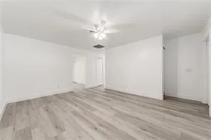a view of an empty room with wooden floor and a ceiling fan
