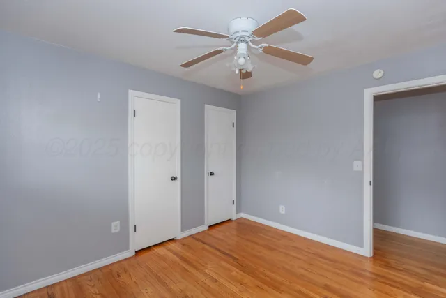an empty room with wooden floor and ceiling fan