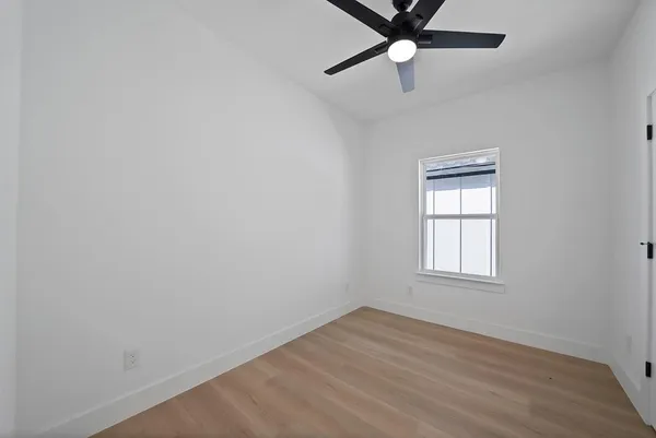an empty room with wooden floor fan and windows