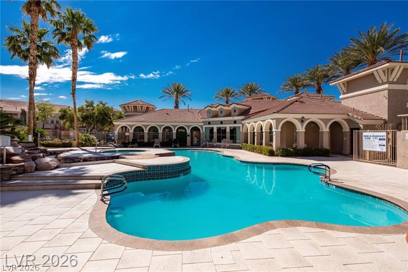 10550 West Alexander Road, Unit 2148 Las Vegas, NV 89129 - Photo 17 of 41 A resort-style pool with a curved design sits adjacent to a charming clubhouse, all framed by towering palm trees.