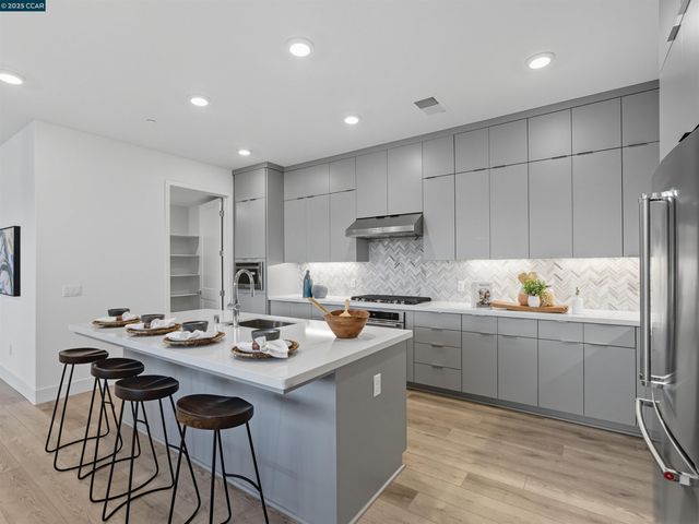 a kitchen with stainless steel appliances granite countertop a stove a sink a refrigerator and white cabinets with wooden floor