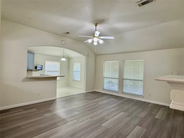an empty room with wooden floor chandelier fan and windows
