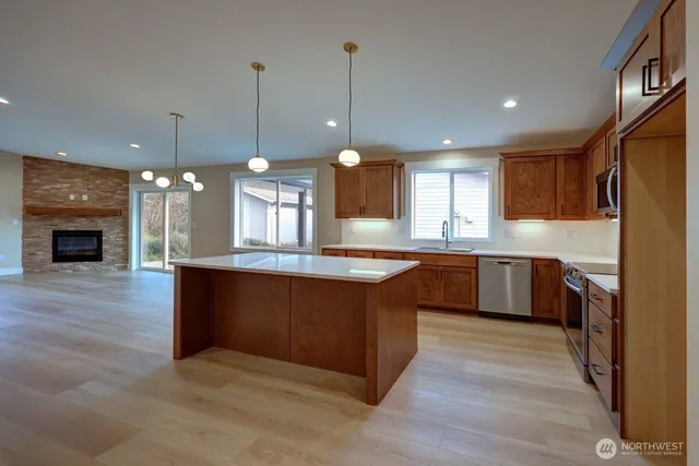 a large kitchen with stainless steel appliances granite countertop a stove a sink dishwasher a refrigerator and a wooden floor