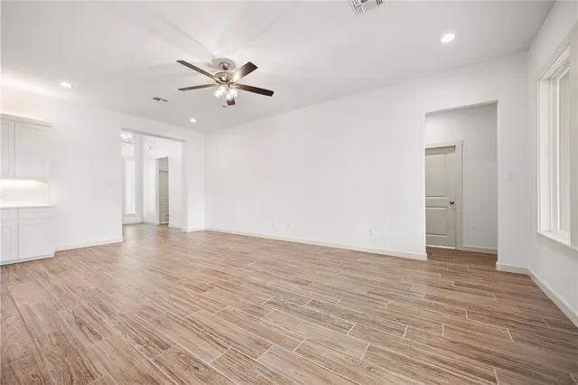 a view of an empty room with wooden floor and a ceiling fan
