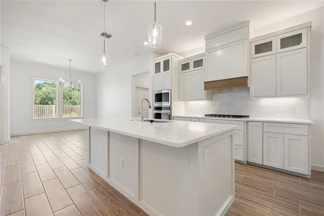 a kitchen with stainless steel appliances granite countertop a sink a stove a refrigerator and white cabinets with wooden floor