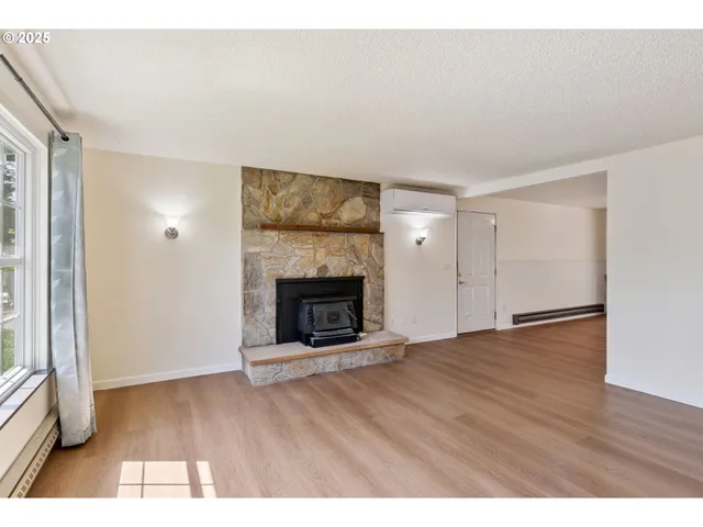 a view of an empty room with wooden floor fireplace and a window