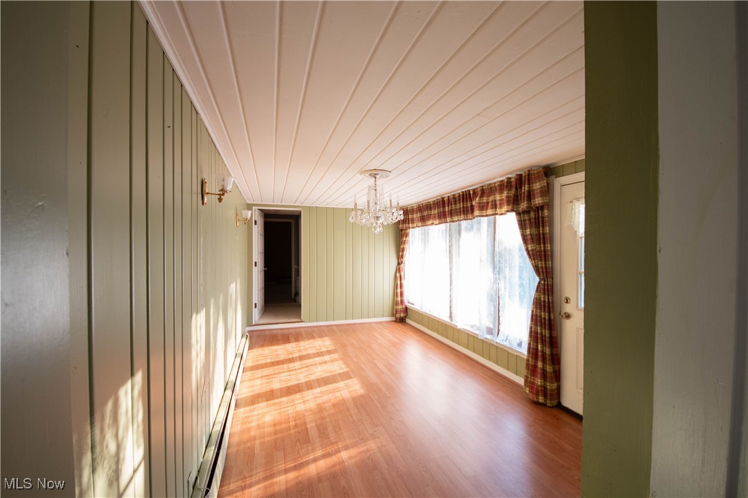 9719 Angling Road Wakeman, OH 44889 - Photo 15 of 39 Empty room featuring a chandelier, a baseboard radiator, wooden walls, wood finished floors, and wood ceiling