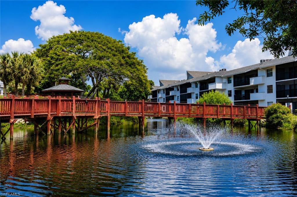600 Neapolitan Way, Unit 449 Naples, FL 34103 - Photo 40 of 44 Community pond with a central fountain, bordered by a wooden pedestrian bridge with red railings