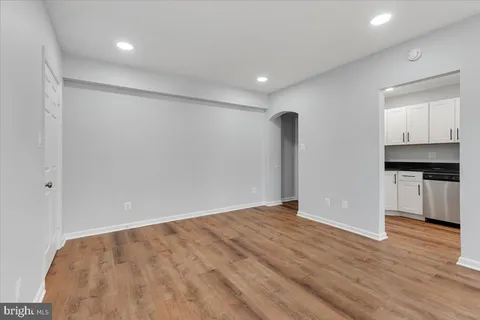 a view of an empty room with wooden floor and a kitchen