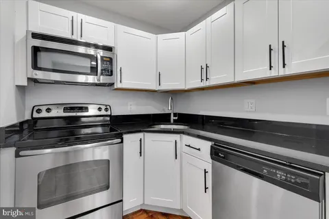 a kitchen with stainless steel appliances granite countertop white cabinets and a stove top oven