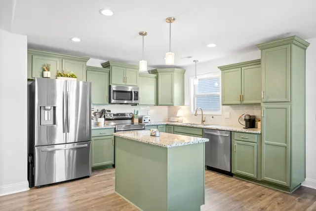 a kitchen with stainless steel appliances granite countertop a refrigerator a sink dishwasher a stove and white cabinets with wooden floor