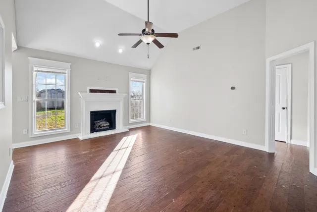 a view of an empty room with wooden floor fireplace and a window
