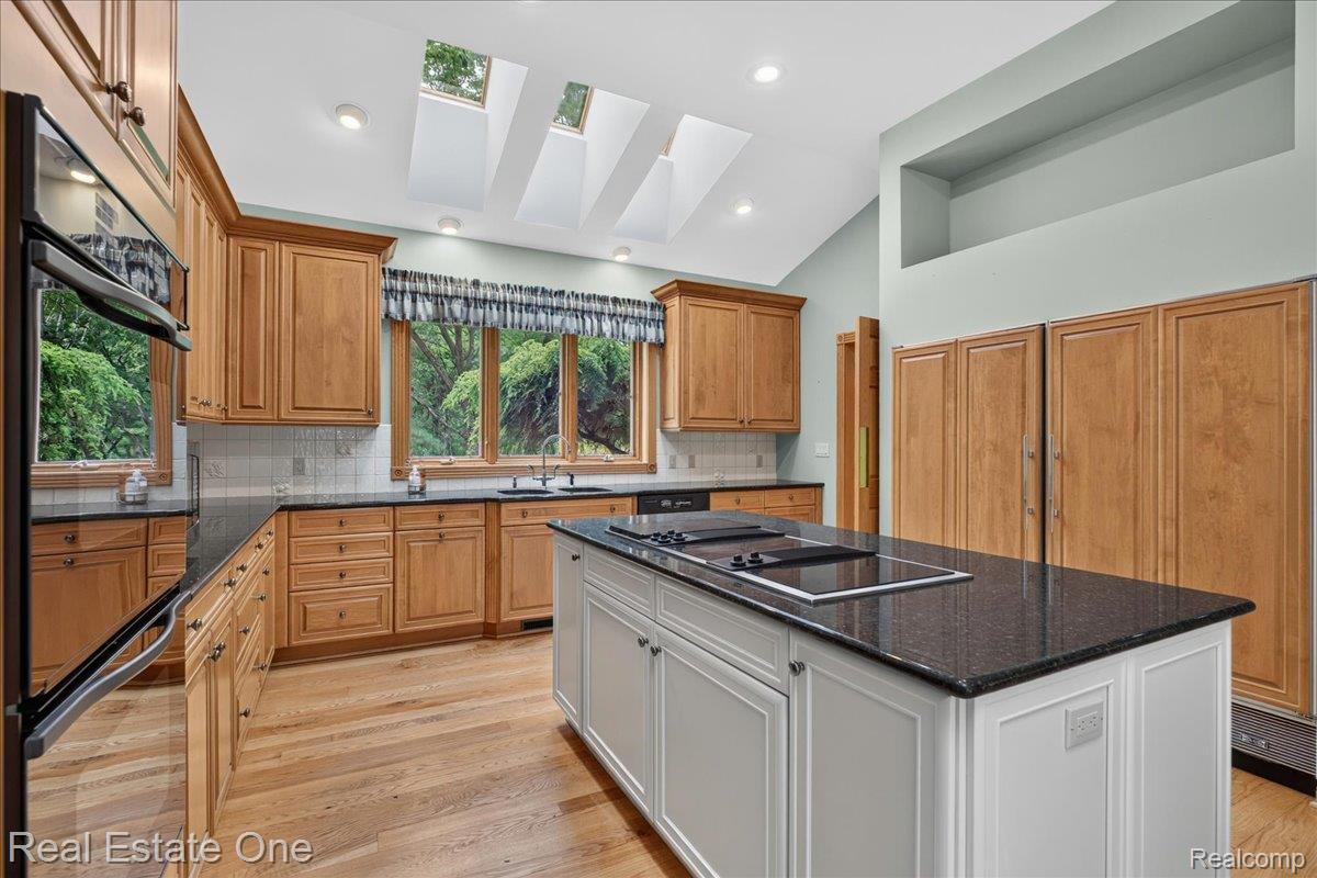 425 Courtney Road Leonard, MI 48367 - Photo 22 of 89 Kitchen with wood-finish cabinetry, black countertops, wood-finish flooring, and multiple skylights