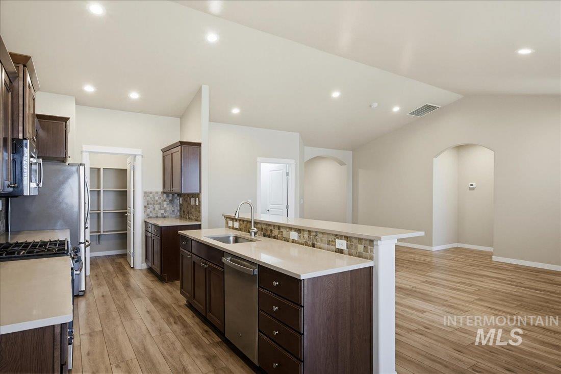 12460 West Azure Street Boise, ID 83713 - Photo 10 of 34 Kitchen featuring wood-finish flooring, dark wood cabinetry, a mosaic tile backsplash, and light-toned countertops