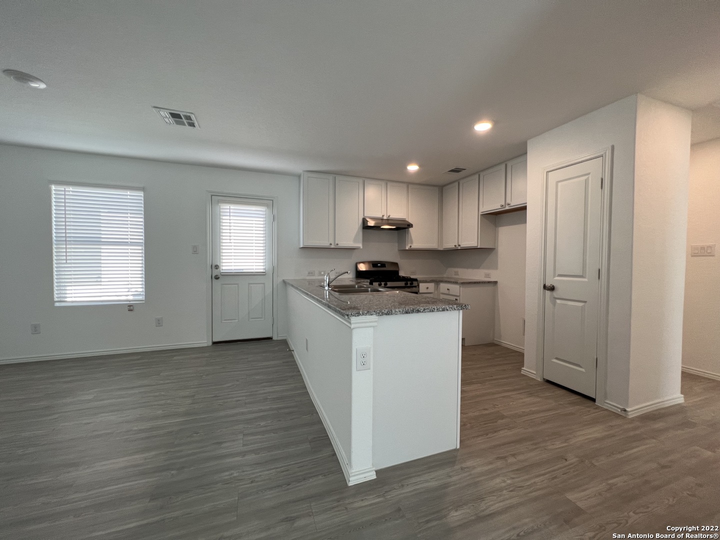 7314 Silos Ridge San Antonio, TX 78252 - Photo 8 of 45 a kitchen with granite countertop wooden floors white cabinets and black appliances