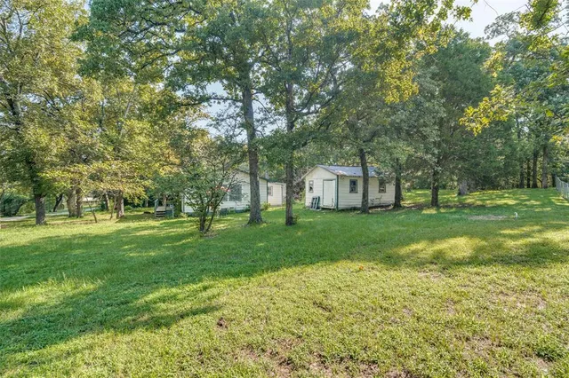 a view of a white house in front of a big yard with large trees