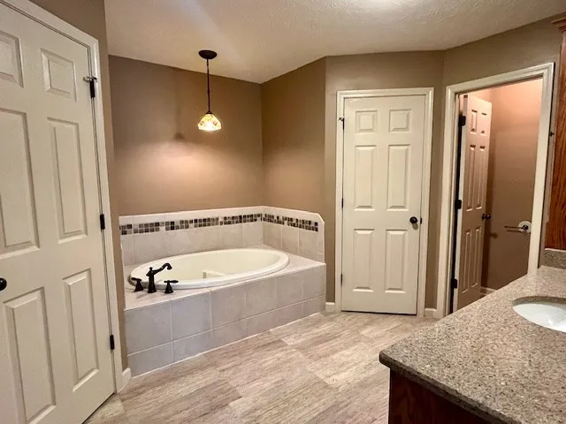 a spacious bathroom with a granite countertop sink a mirror and a bathtub