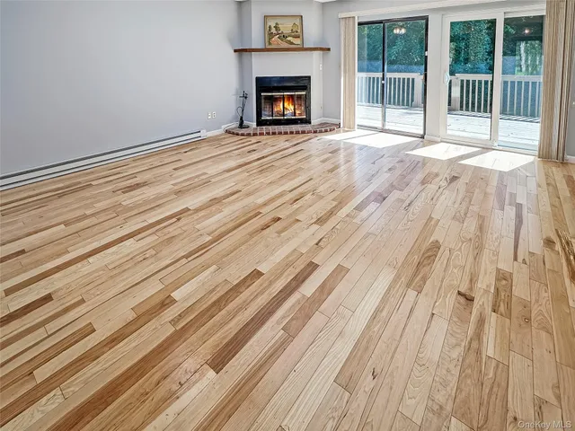 a view of an empty room with wooden floor fireplace and a window