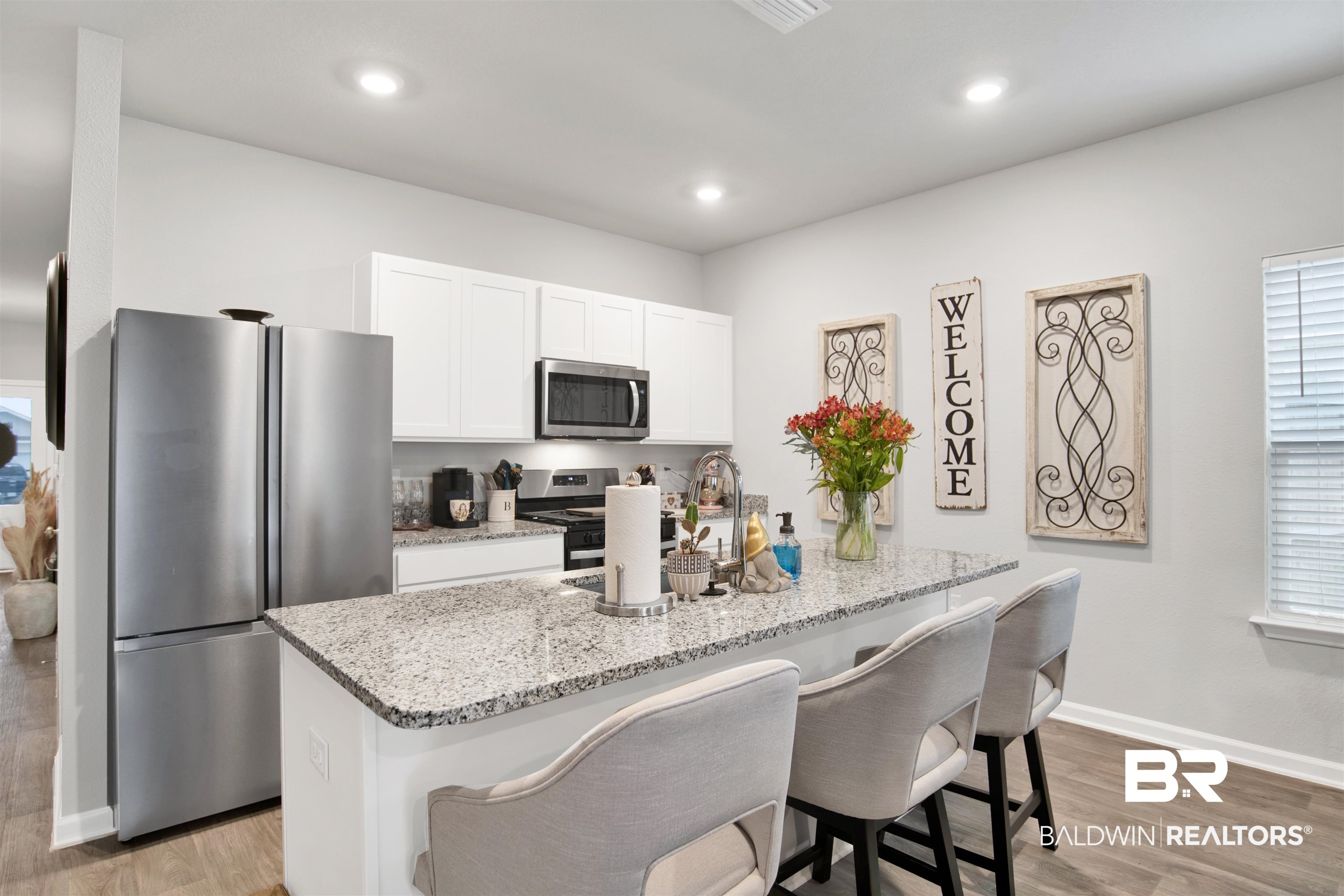 12813 Patriot Way Daphne, AL 36527 - Photo 4 of 23 Kitchen featuring an island with a light-toned granite countertop, white cabinetry, stainless steel appliances, and wood-finish flooring